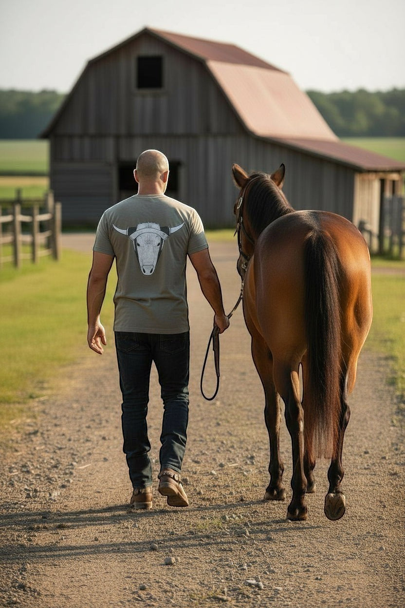 Haze N Handle unisex gray cotton tee with steer head graphic on back and small chest logo. Model walking horse near barn.